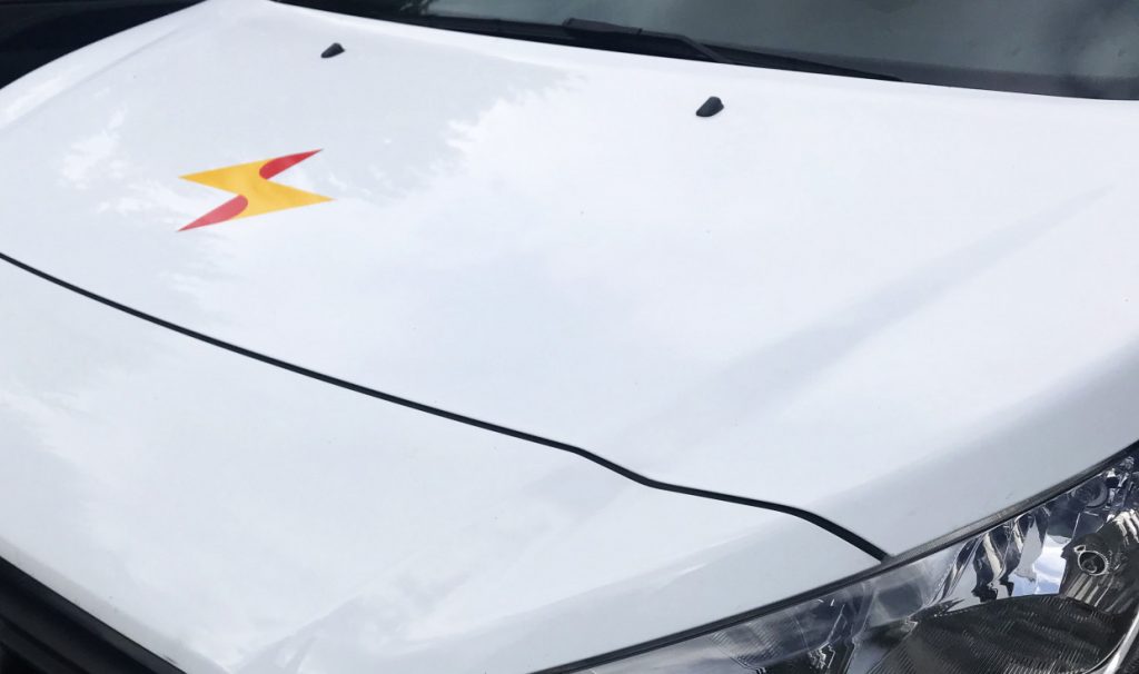 Studioviv levert opvallende voertuigbelettering zoals deze reed en gele bliksemflits op een witte motorkap.